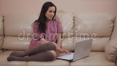 年轻<strong>的</strong>布鲁内特女孩在<strong>温暖的</strong>袜子，躺在皮革沙发在<strong>家</strong>里和工作在笔记本电脑